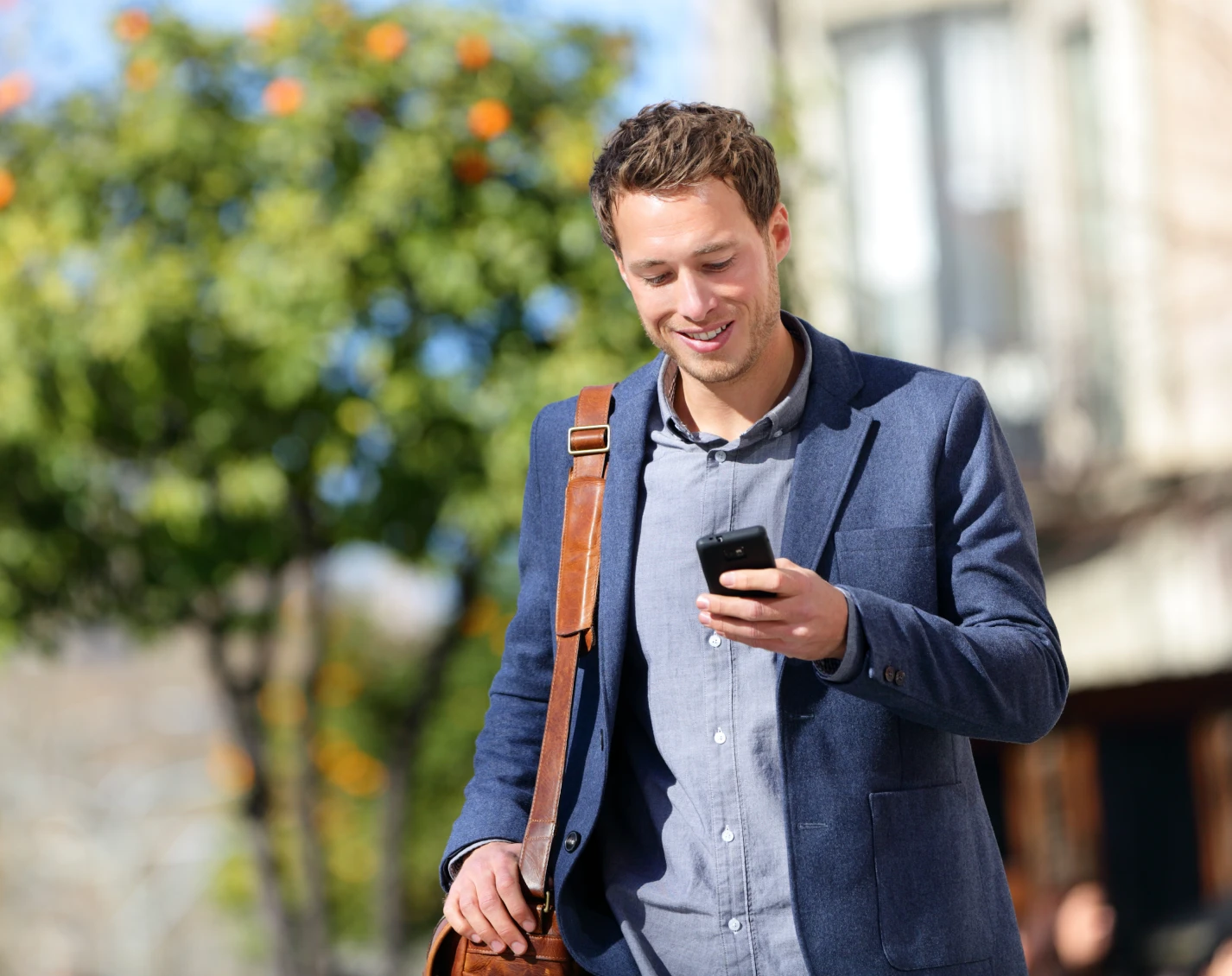 Young professional walking outside enjoying green space while checking phone on a sunny day