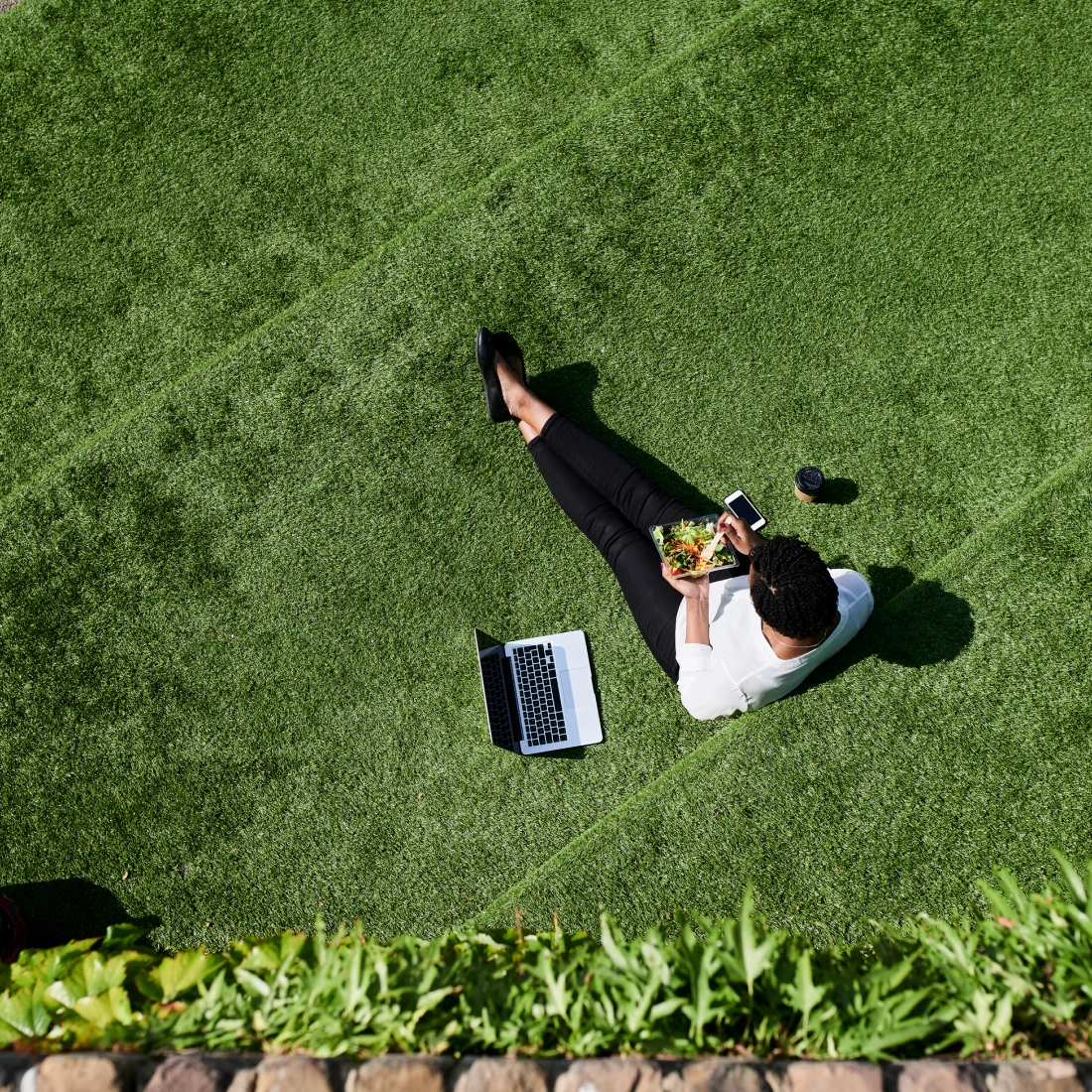 Professional enjoying lunch on landscaped green space with laptop and coffee
