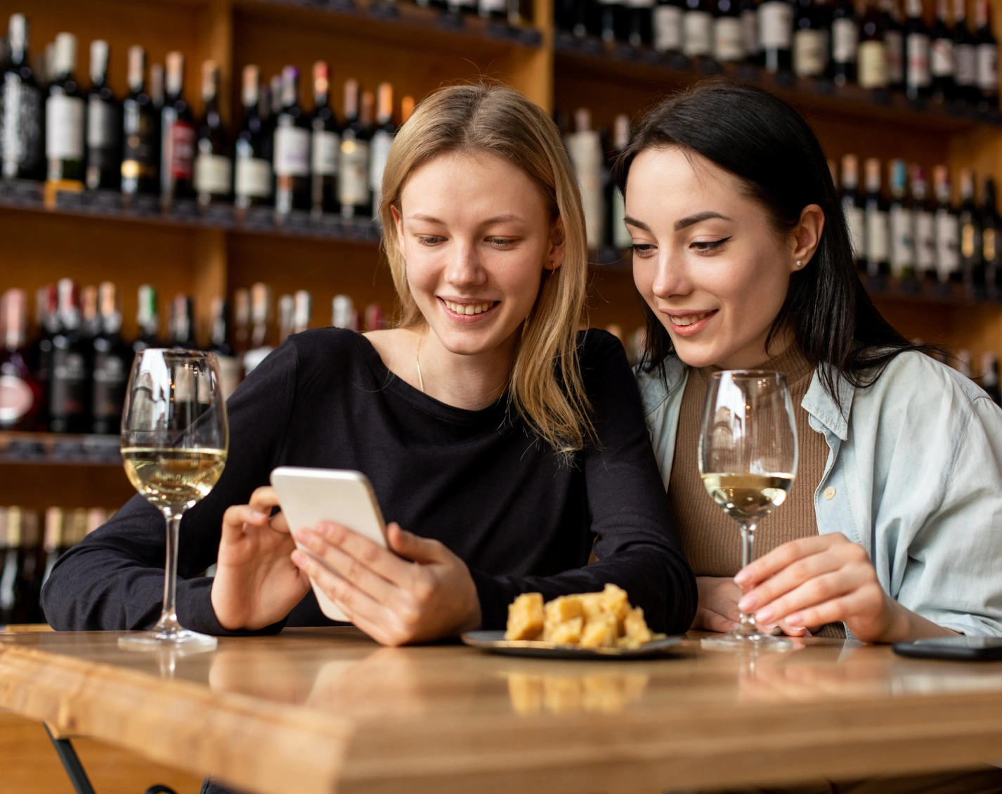 Friends sharing appetizers and wine inside stylish restaurant with bottle lined shelves