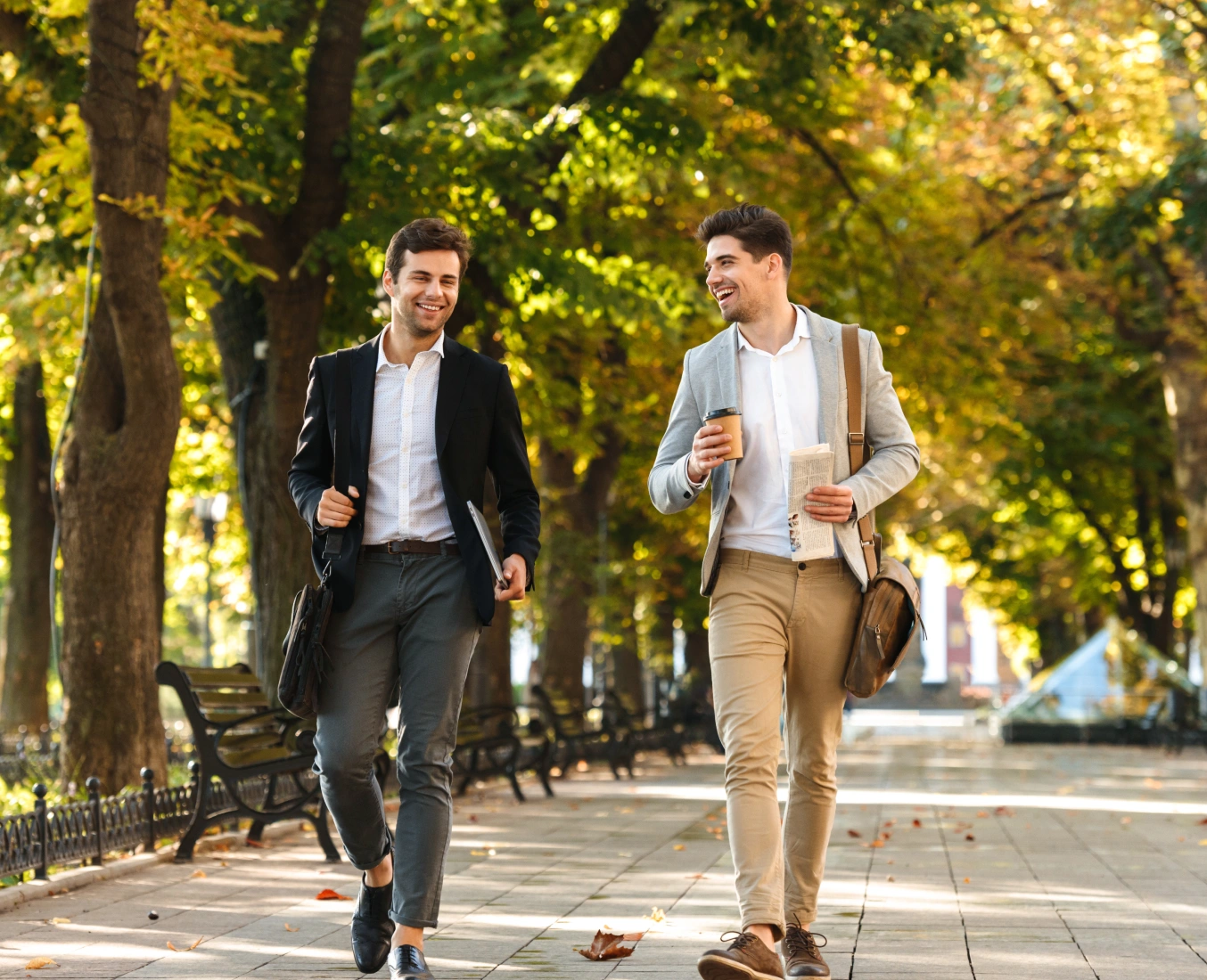 Young professionals in business attire strolling along sunny urban park pathway